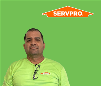 SERVPRO employee with dark hair wearing a green shirt in front of a green background