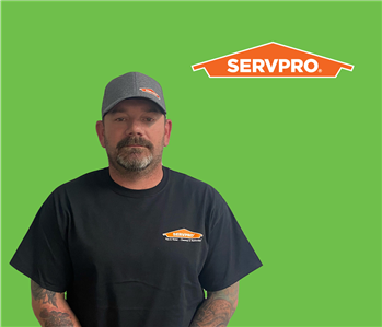 SERVPRO employee with a hat wearing a black shirt in front of a green background