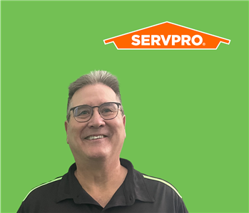 SERVPRO employee with light hair wearing a black shirt in front of a green background